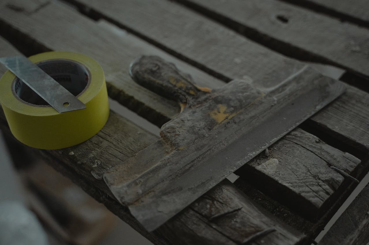Close-up of a spatula and duct tape on an aged wooden surface. Perfect for DIY and renovation themes.