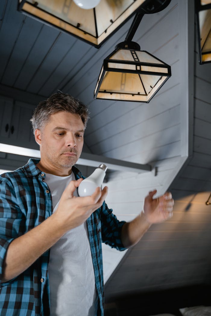 Man in a plaid shirt replaces a light bulb in a modern, stylish home interior.